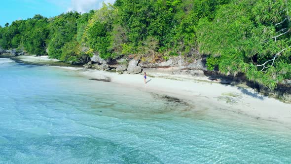Aerial: woman walking on desert beach, tropical island white sand beach turquoise caribbean sea