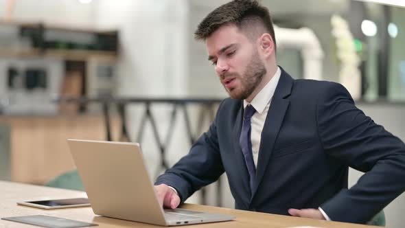 Tired Young Businessman with Laptop Having Neck Pain in Office