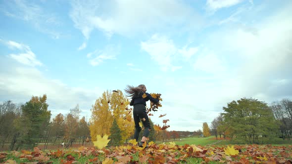 A Young Girl Schoolgirl Whirls with Autumn Leaves in the City Park