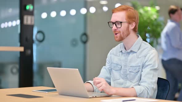 Cheerful Young Redhead Man Talking on Video Call on Laptop in Office