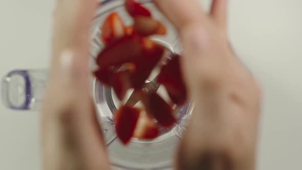 Pieces of strawberry fall into mixer from a hands