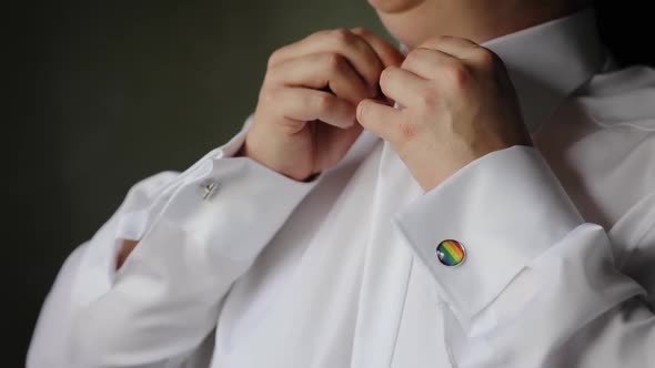 Close-up of person dressing white shirt. Cufflink emblem with pride rainbow flag. LGBT wedding