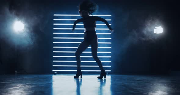 Silhouette Figure of a Dancing Girl in the Dark on Heels and Short Shorts