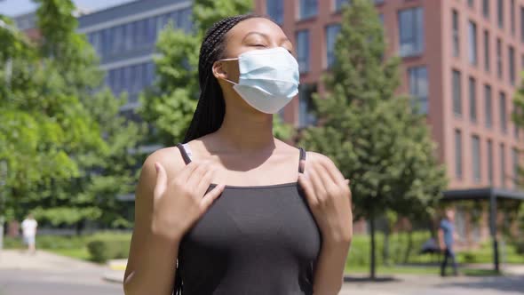 A Young Black Woman in a Face Mask Celebrates - an Office Building and Trees in an Urban Area