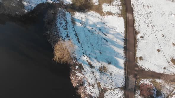 Aerial footage camera tilting up at a lake spring starting, snow and grass