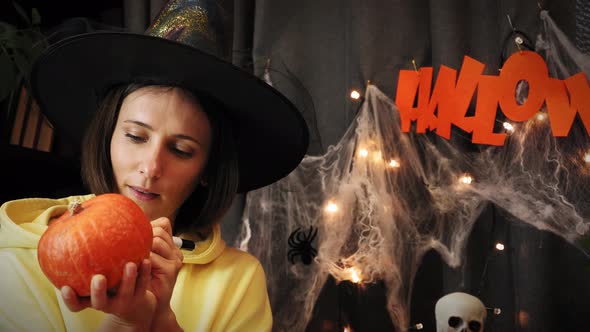 Halloween. Woman in witch hat painting orange pumpkin face