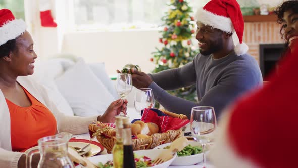 African american man in santa hat pouring drink in glass of senior woman while sitting on dining tab