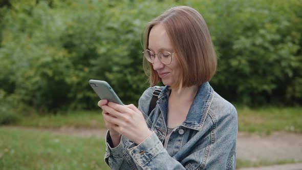 Cheerful Girl Student 20s 30s in Glasses Chatting Online Uses Smartphone Social Media Paying Online