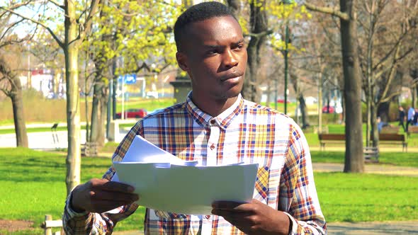 A Young Black Man Does Paperwork in a Park on a Sunny Day
