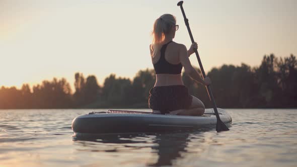 Girl Floating On Sup Board At Idyllic Evening. Swimming On Stand Up Paddle Board. Surfer Water Sport
