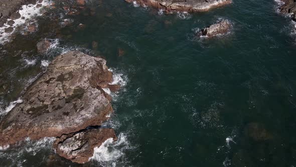 downward tilted drone footage of the Pacific Ocean pounding the coastal rocks on a tropical island