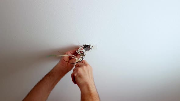 Screwing on a mount for a ceiling light with wires sticking out from a hole