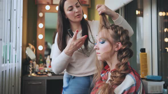The Girl Makeup Artist Makes a Braid for the Model