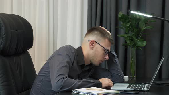 Frustrated male is working alone, falling asleep at workplace, Sleepy man is overwhelmed with work