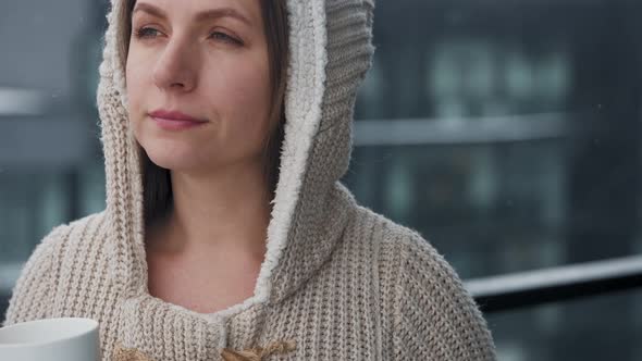 Caucasian Woman Stays on Balcony During Snowfall with Cup of Hot Coffee or Tea