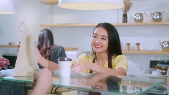 Attractive asian female cafe worker  giving takeaway food bag to customer.