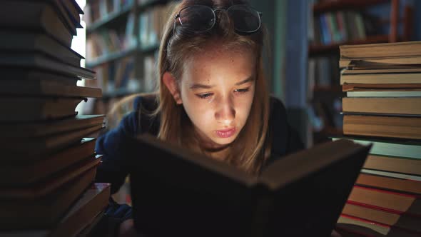 Girl is Sitting in Library Between the Bookshelves and Reading Book Aloud for Finding Information