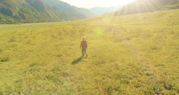 Flight Over Backpack Hiking Tourist Walking Across Green Mountain Field. Huge Rural Valley at Summer