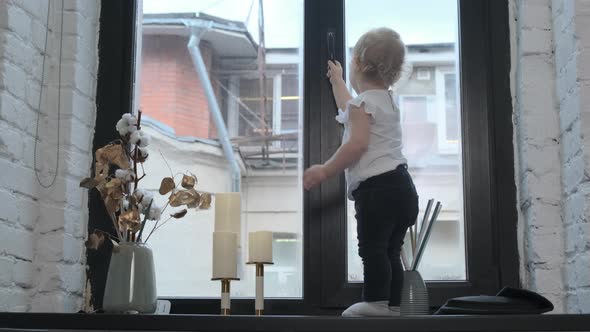 Little Cute Funny Child Girl in White T-shirt and Dark Pants Is Dancing on Windowsill in the