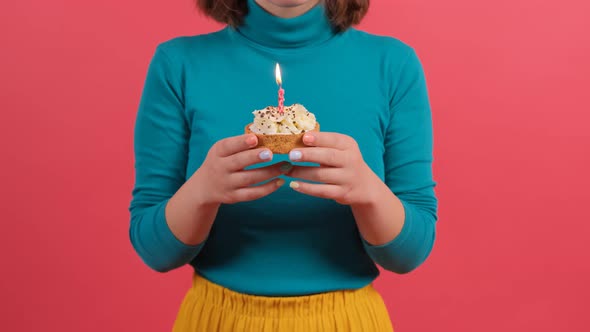Young Woman Blowing Out Candle on Cake, Isolated on Red Background.