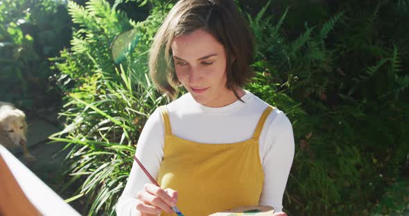 Smiling caucasian woman with brown hair painting in sunny garden