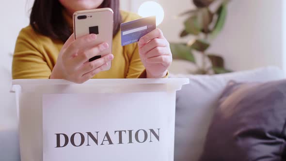 Detail of female hands making a donation with a credit card and clothes into the box for the donat.