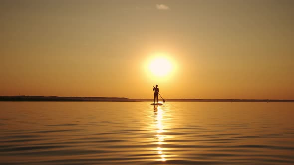 Woman Standing Firmly on Inflatable SUP Board and Paddling Through Shining Water Surface