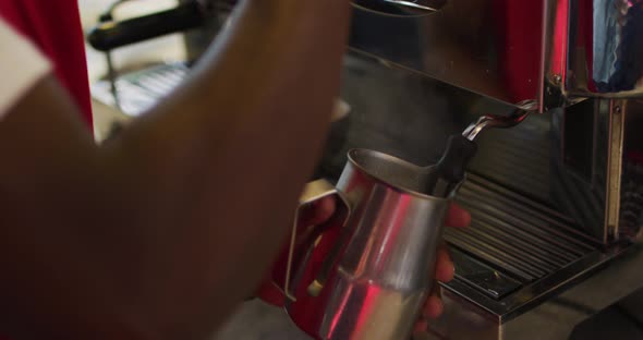 Midsection of african american barista using coffee machine frothing milk in cafe