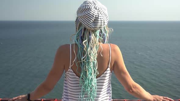 A Beautiful Young Woman Looks From a Height at the Blue Transparent Sea on a Sunny Day