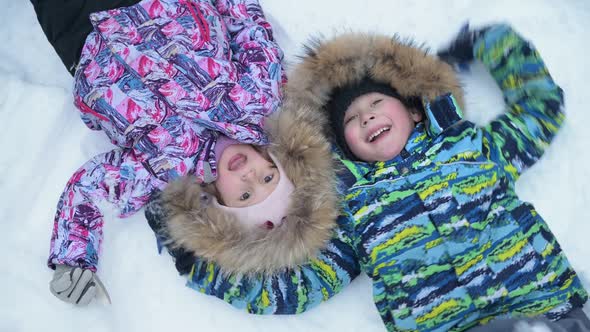 Two children, sister and brother are lying in the snow and fooling around