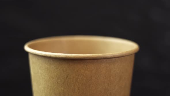 A Cardboard Cup Made of Rapidly Degradable Material Spins on a Black Background