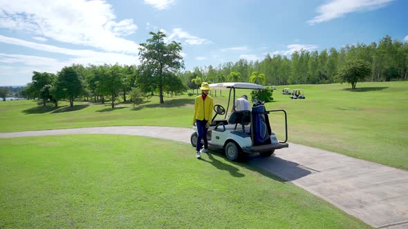 4K Asian senior man driving golf cart on golf course to golfing on the green with female caddy