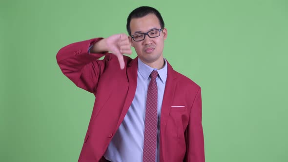 Sad Asian Businessman with Eyeglasses Giving Thumbs Down