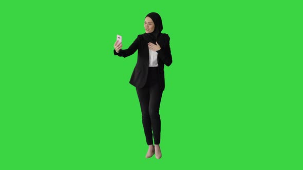 Young Pretty Muslim Woman in Hijab Having Video Call on Her Phone As She Walks on a Green Screen