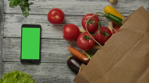 Two Fresh Tomatoes Rolling Near Vegetables and Smartphone