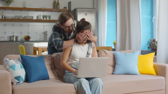 Young Woman Working on Laptop When Boyfriend Closing Her Eyes.