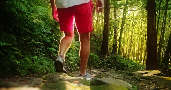 Guy in Red Shorts and White Tshirt Walks Along Steep Hill Covered in Moss