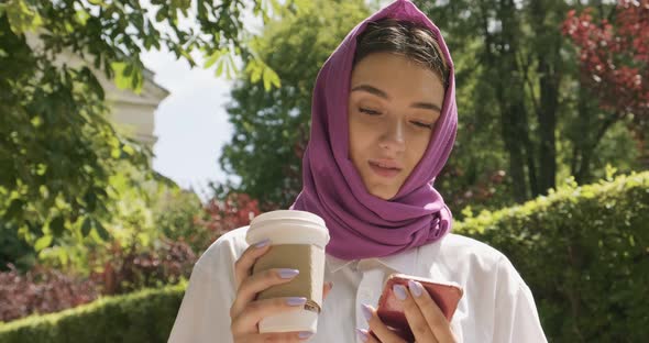 Beautiful Young Woman Drink Coffee and Looking at Smartphone, Wearing Traditional Headscarf