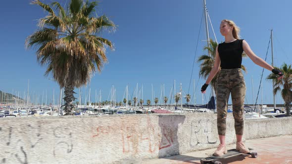 A Beautiful Blonde Girl on Skateboard in Summer Hot Day on Seafront