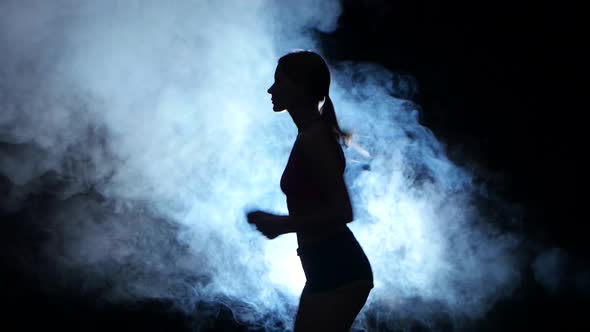 Athletic Fitness Girl Running on a Black Background Illuminated By the Spotlight in the Smoke