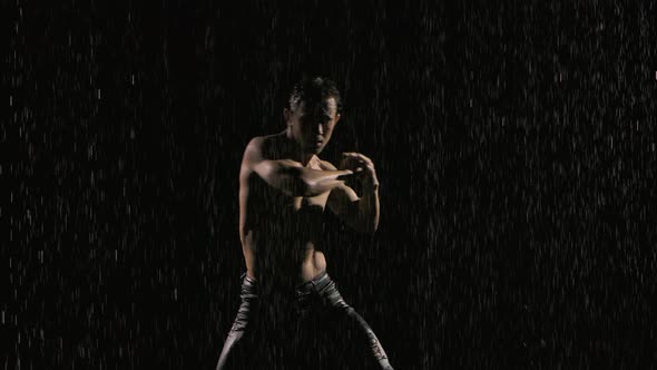 Young Attractive Man with a Naked Torso Dances Sexually in the Rain in a Dark Studio. Silhouettes