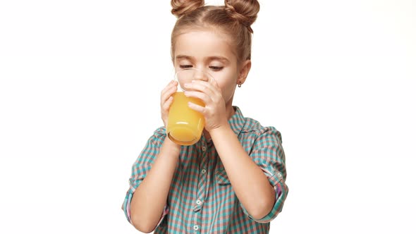 Cute Small Caucasian Girl Kid in Plaid Shirt and Hair Buns Drinking Orange Juice From Glass and