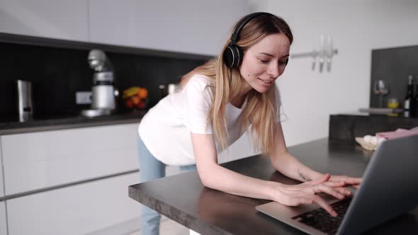 Woman Spending Time with Laptop Wearing Headphones in Kitchen