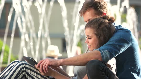 Young Loving Couple Sitting By the Beautiful Fountain