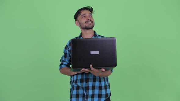 Happy Young Bearded Persian Hipster Man Thinking While Using Laptop