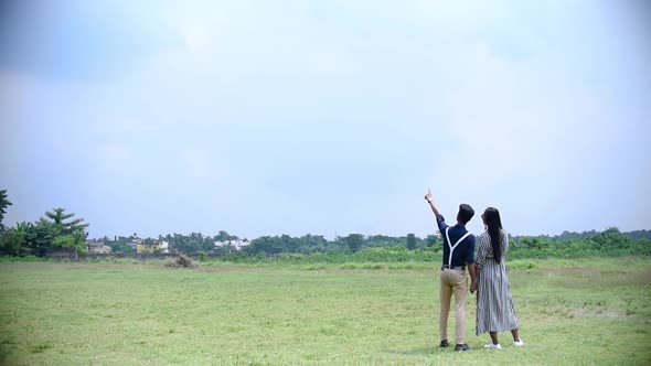 Romantic couple looking at field or grassland and sky, planning future house at construction locatio