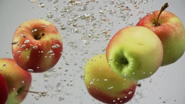 Yummy Fresh Apples Red and Yellow Falling in Water Spinning Rotating Air Bubbles White Background