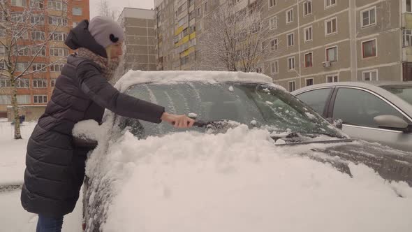 A woman cleans the car from snow after a snowstorm with a brush