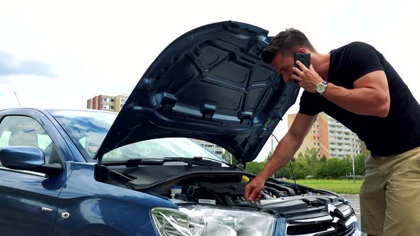 Young Handsome Man Looks on Engine in Car and Phone with Smartphone - Accident 