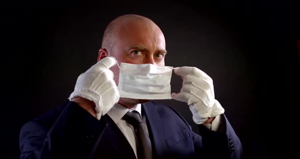 Portrait of a Man in a Business Suit and White Protective Gloves on a Black Background. He Puts on a